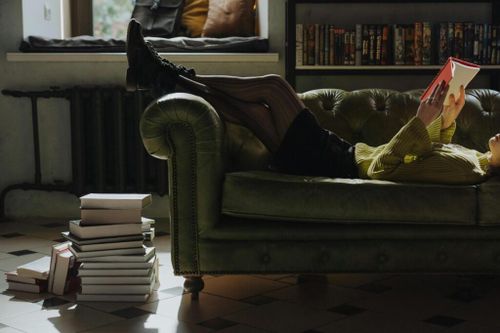 Women on Sofa reading a book. The face is not shown, the sofa is green leather.